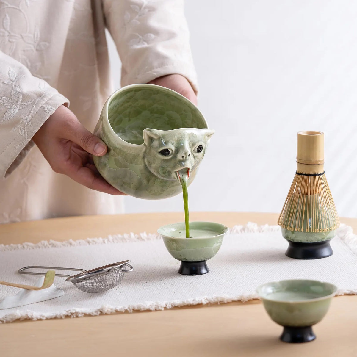 Matcha pouring from the cat's mouth spout into a cup